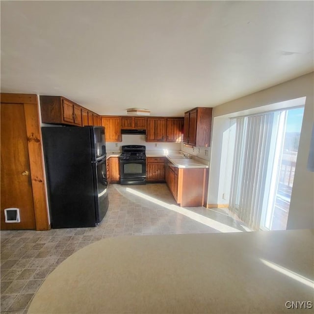 kitchen with under cabinet range hood, a sink, light countertops, black appliances, and brown cabinetry