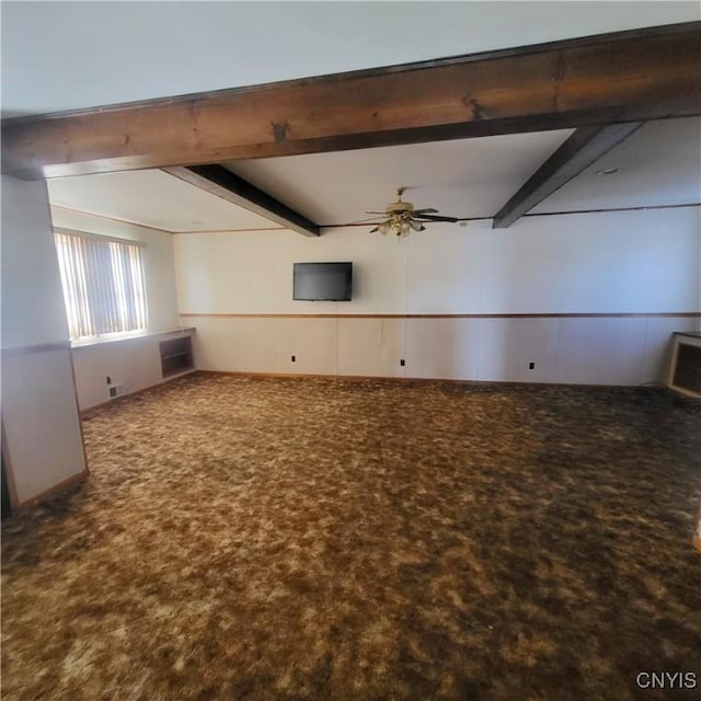 spare room featuring a wainscoted wall, beamed ceiling, carpet flooring, and a ceiling fan