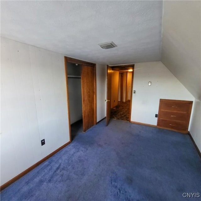 unfurnished bedroom featuring baseboards, visible vents, a textured ceiling, dark carpet, and a closet