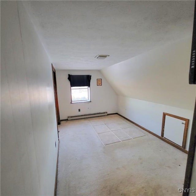 additional living space featuring a baseboard heating unit, vaulted ceiling, a textured ceiling, and visible vents