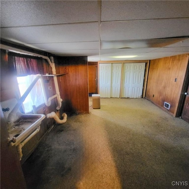 below grade area with carpet, a drop ceiling, wood walls, and visible vents