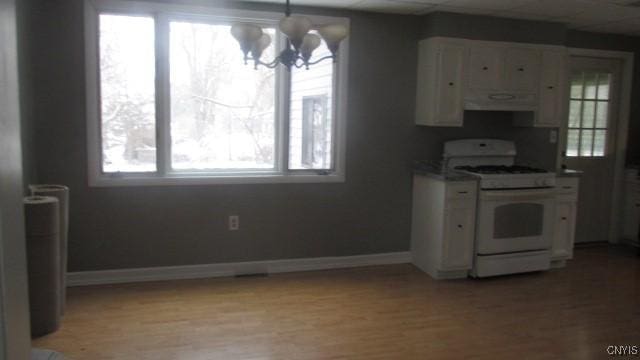 kitchen featuring white cabinetry, white range with gas stovetop, a healthy amount of sunlight, and a chandelier