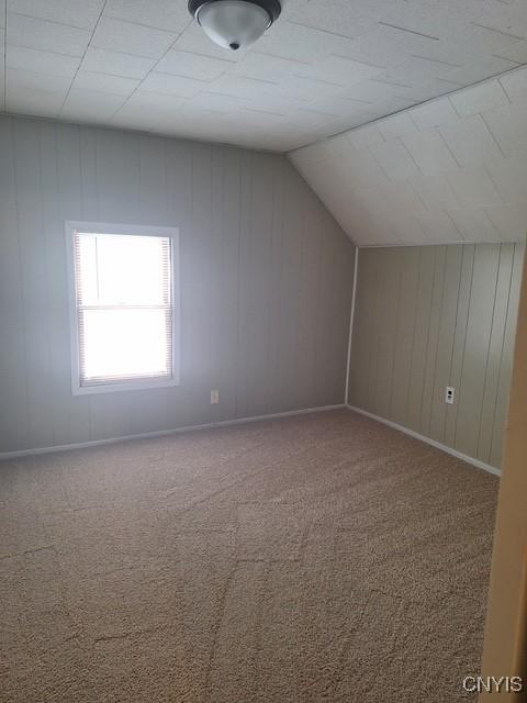 additional living space featuring carpet floors, lofted ceiling, and wood walls