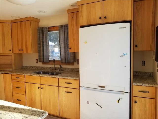 kitchen featuring light stone countertops, white fridge, and sink