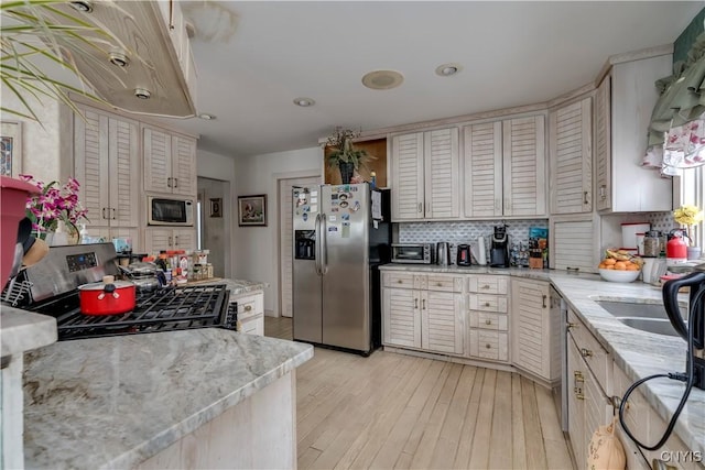 kitchen featuring light stone countertops, light wood-type flooring, appliances with stainless steel finishes, and tasteful backsplash