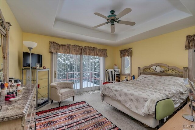 carpeted bedroom with a tray ceiling, ceiling fan, and access to outside