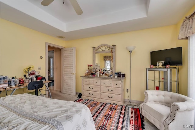 bedroom with a raised ceiling, ceiling fan, and carpet flooring