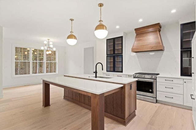 kitchen featuring sink, an island with sink, stainless steel range, light hardwood / wood-style floors, and custom range hood