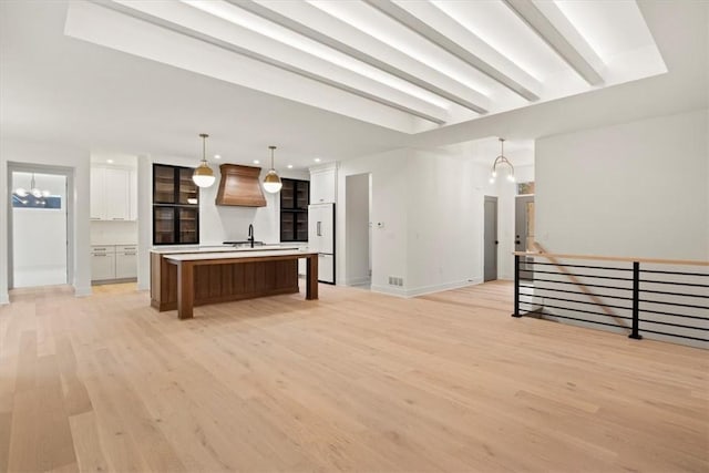 kitchen with white refrigerator, decorative light fixtures, an inviting chandelier, white cabinets, and an island with sink