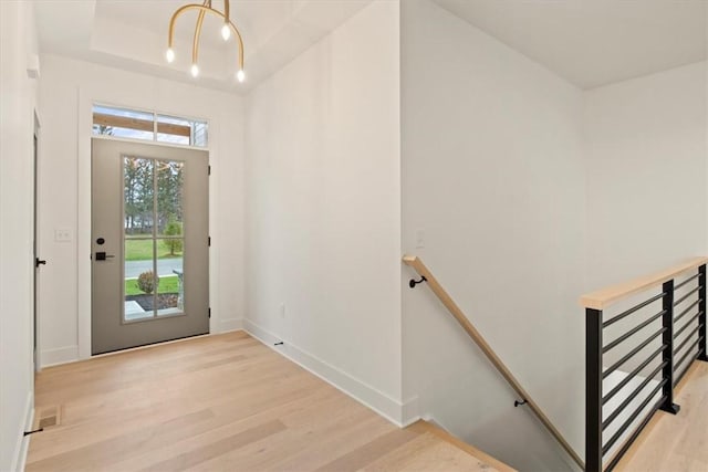 interior space with light hardwood / wood-style floors, a raised ceiling, and a notable chandelier