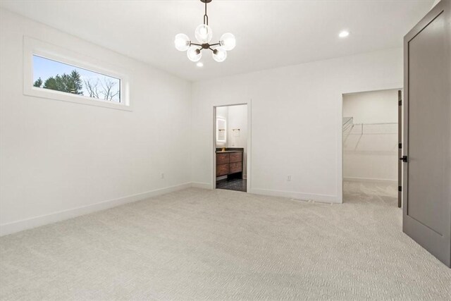 unfurnished bedroom featuring light carpet, an inviting chandelier, a spacious closet, connected bathroom, and a closet