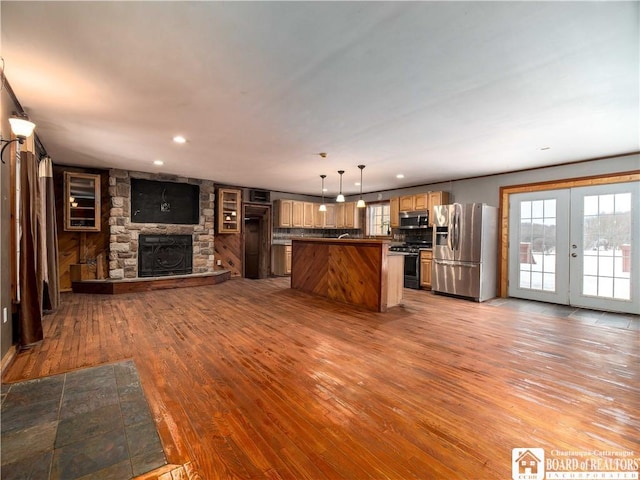 kitchen with appliances with stainless steel finishes, light wood-type flooring, decorative light fixtures, a fireplace, and a kitchen island