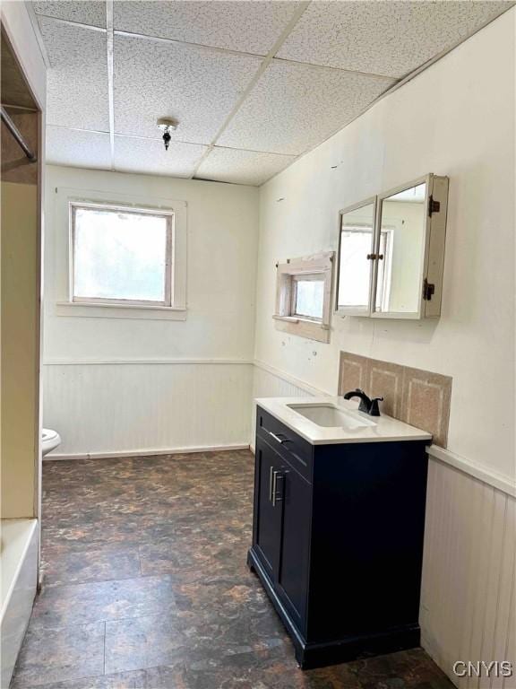 kitchen with a drop ceiling, sink, and wooden walls