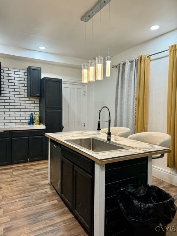 kitchen featuring dishwasher, sink, hanging light fixtures, an island with sink, and light hardwood / wood-style floors