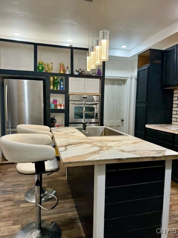 bar with light stone countertops, stainless steel fridge, dark wood-type flooring, and decorative light fixtures