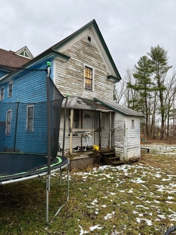 snow covered back of property with a trampoline and a sunroom