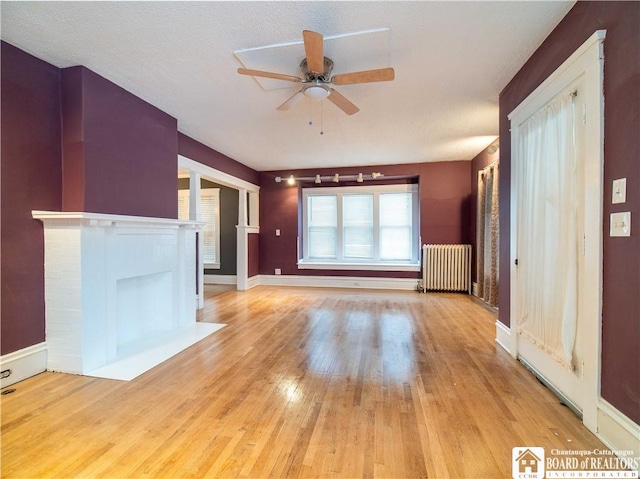 unfurnished living room featuring a textured ceiling, light hardwood / wood-style floors, radiator, and ceiling fan