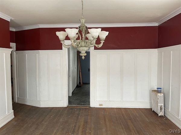 unfurnished dining area featuring dark hardwood / wood-style flooring, crown molding, radiator, and a notable chandelier