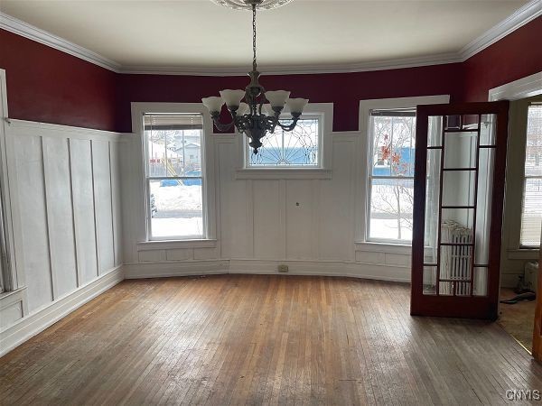 unfurnished dining area with hardwood / wood-style flooring, crown molding, and a chandelier