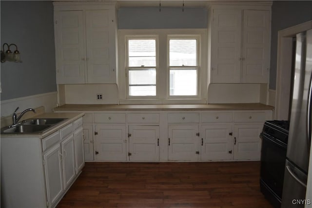 kitchen with black range oven, sink, white cabinets, dark hardwood / wood-style floors, and stainless steel refrigerator