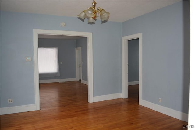 empty room with hardwood / wood-style floors and a notable chandelier