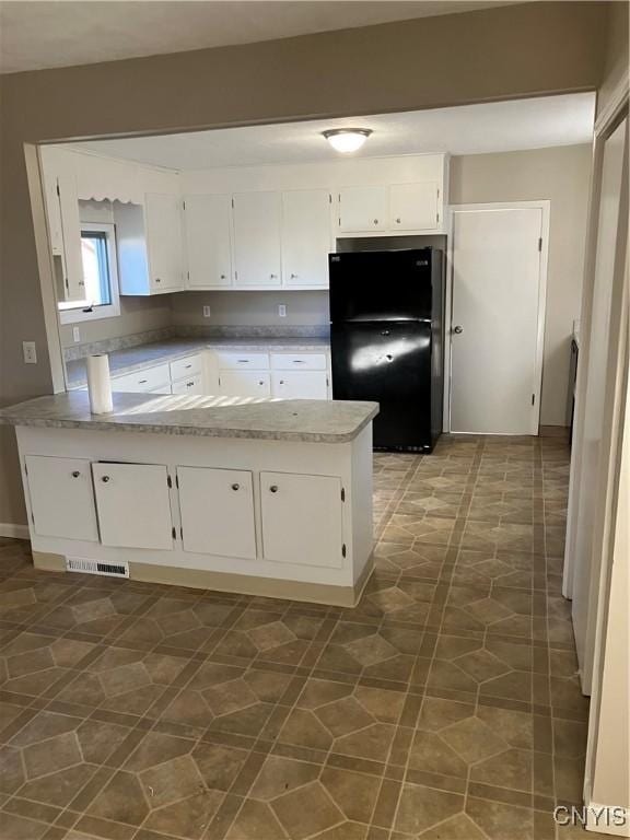 kitchen featuring kitchen peninsula, light stone counters, black refrigerator, and white cabinets