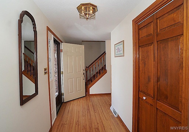 hall featuring light wood-type flooring and a textured ceiling