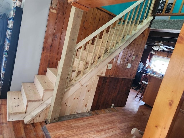 stairs featuring ceiling fan, wood walls, and wood-type flooring
