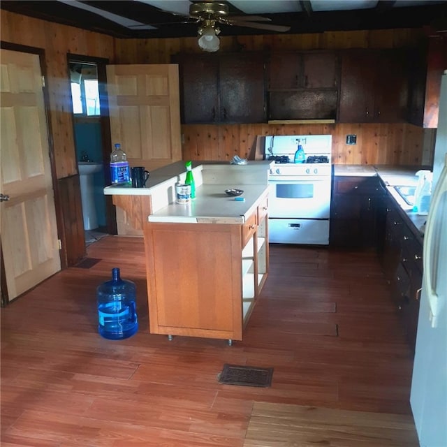 kitchen featuring hardwood / wood-style floors, wood walls, white appliances, ceiling fan, and a kitchen island