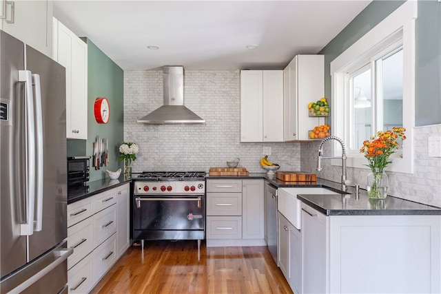 kitchen featuring white cabinetry, sink, wall chimney range hood, decorative backsplash, and appliances with stainless steel finishes