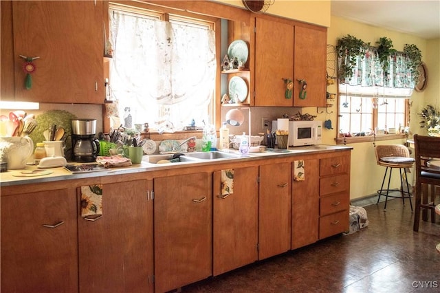 kitchen with light countertops, a sink, open shelves, white microwave, and brown cabinetry