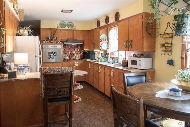 kitchen with white appliances, brown cabinetry, and wall chimney exhaust hood