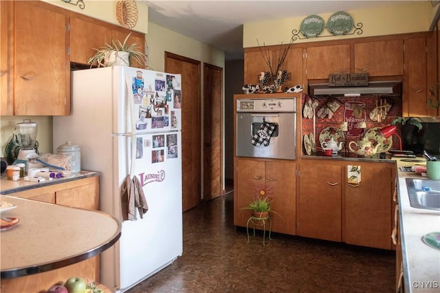 kitchen with under cabinet range hood, freestanding refrigerator, brown cabinetry, and oven