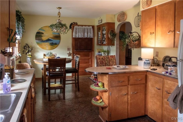 kitchen featuring light countertops, a sink, a peninsula, brown cabinets, and arched walkways