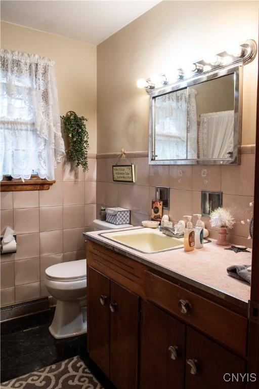 bathroom featuring toilet, vanity, and tile walls