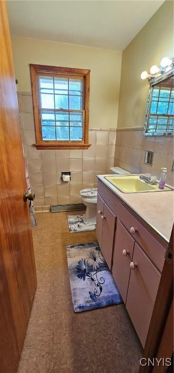 half bath featuring tile walls, toilet, vanity, and wainscoting