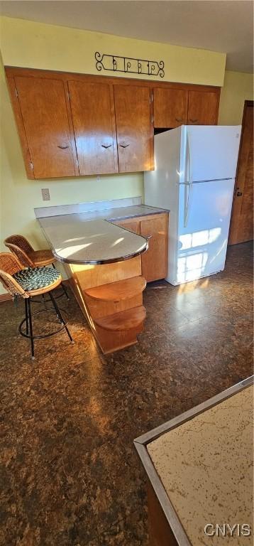 kitchen featuring freestanding refrigerator and brown cabinetry