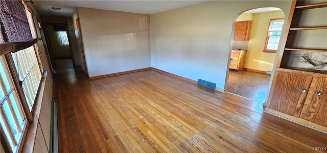 empty room with arched walkways, baseboards, visible vents, and wood finished floors
