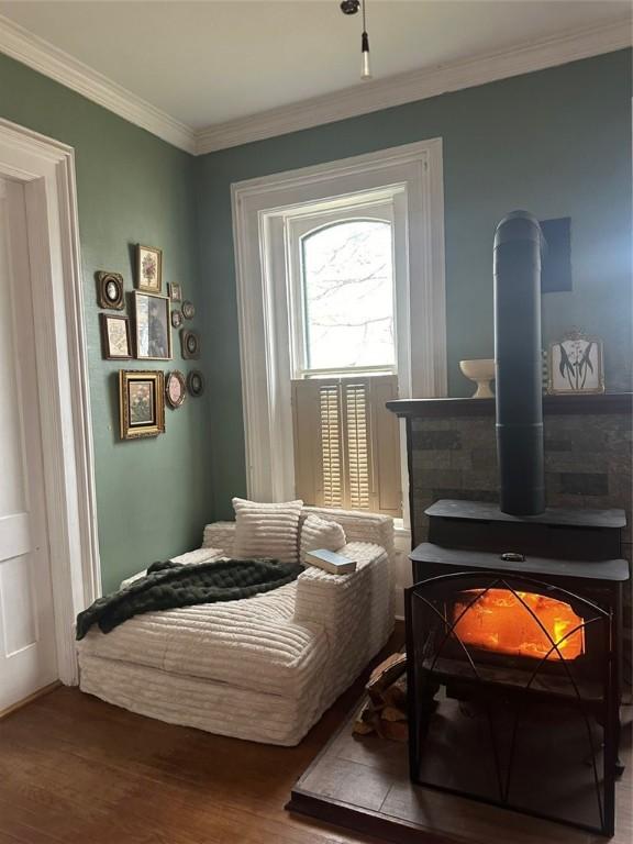 sitting room featuring wood-type flooring, a wood stove, and ornamental molding