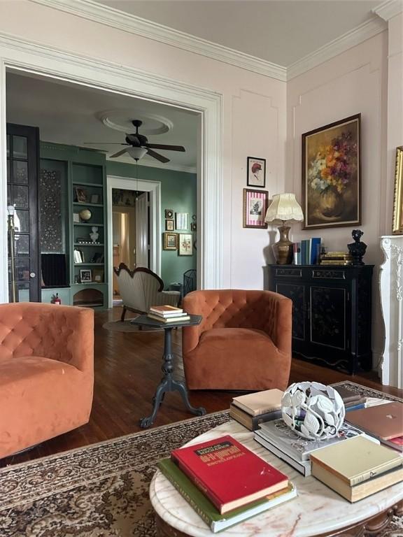 living room featuring built in shelves, ceiling fan, wood-type flooring, and ornamental molding