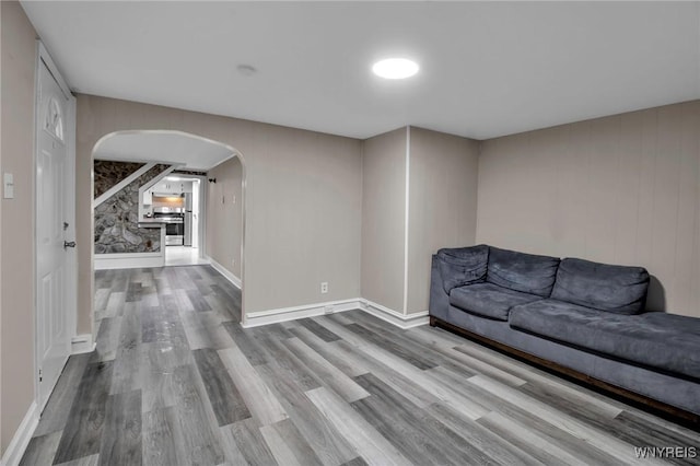 unfurnished living room featuring wood finished floors, arched walkways, and baseboards