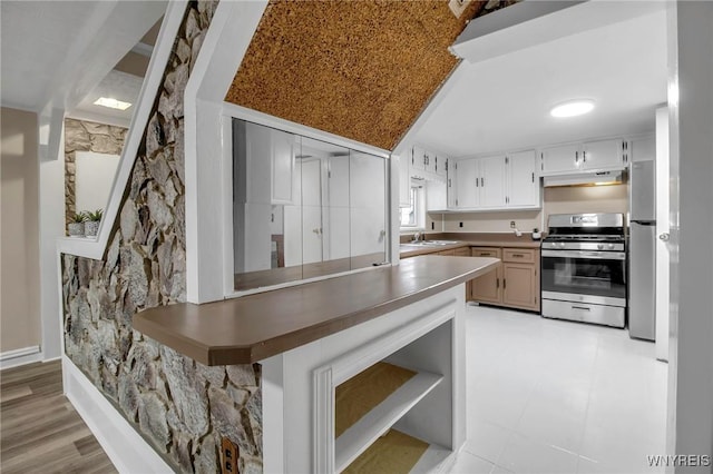 kitchen featuring under cabinet range hood, stainless steel appliances, light floors, and a peninsula