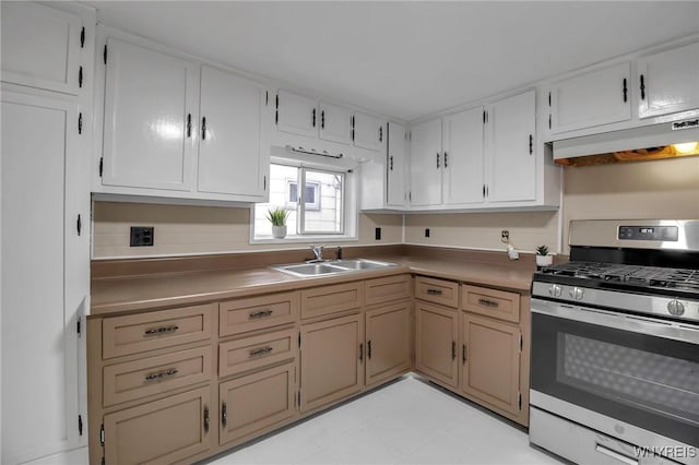 kitchen featuring under cabinet range hood, gas range, white cabinetry, and a sink