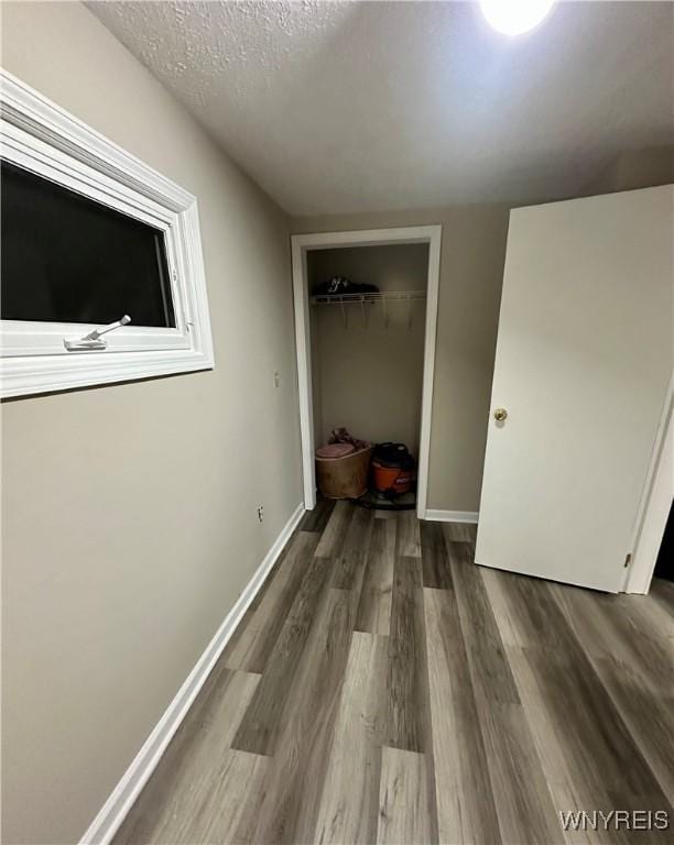 unfurnished bedroom with dark wood-style floors, a closet, a textured ceiling, and baseboards