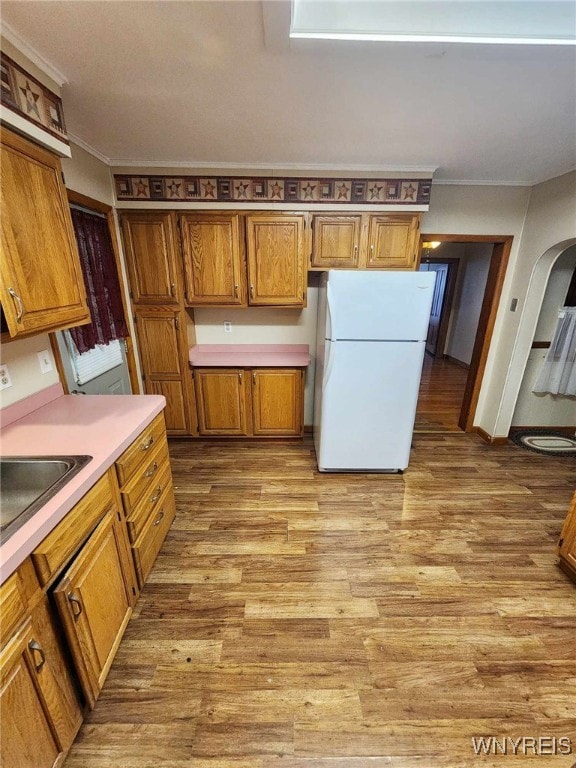 kitchen featuring sink, white fridge, ornamental molding, and light wood-type flooring