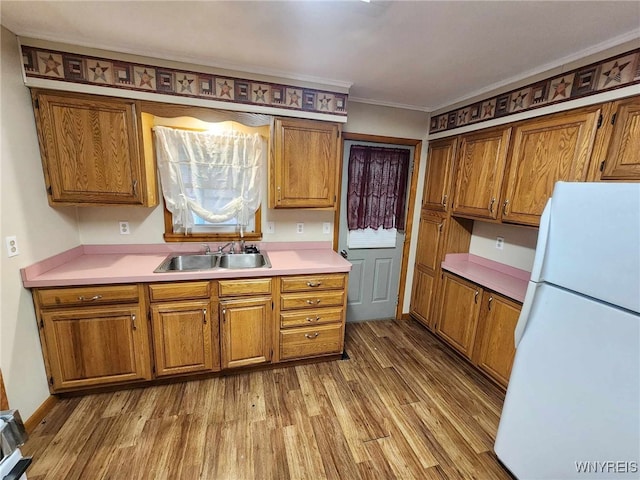 kitchen featuring white refrigerator, hardwood / wood-style flooring, ornamental molding, and sink