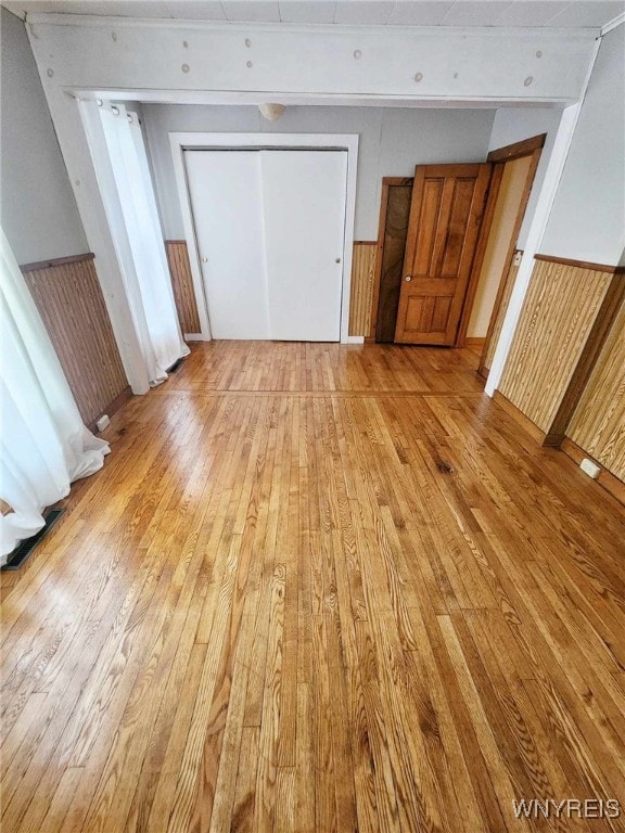 unfurnished bedroom with wooden walls, a closet, and light hardwood / wood-style flooring