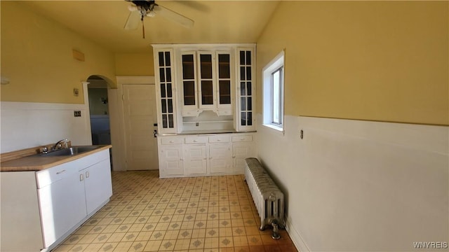 kitchen with white cabinets, ceiling fan, sink, and radiator