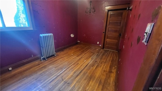 empty room featuring hardwood / wood-style flooring, radiator heating unit, and an inviting chandelier