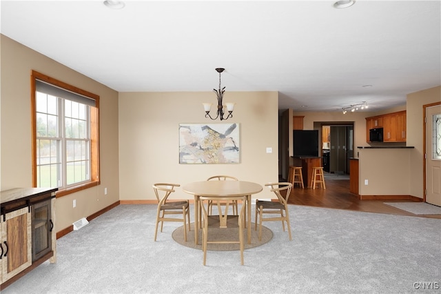 carpeted dining space featuring track lighting and a notable chandelier